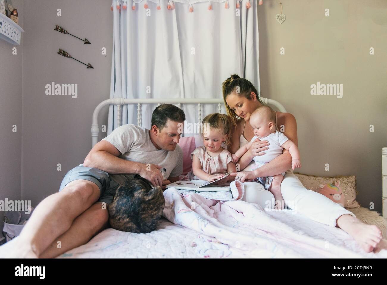 La famille s'asseyant ensemble sur le lit de bébé pendant qu'elle lit l'heure du coucher histoires Banque D'Images