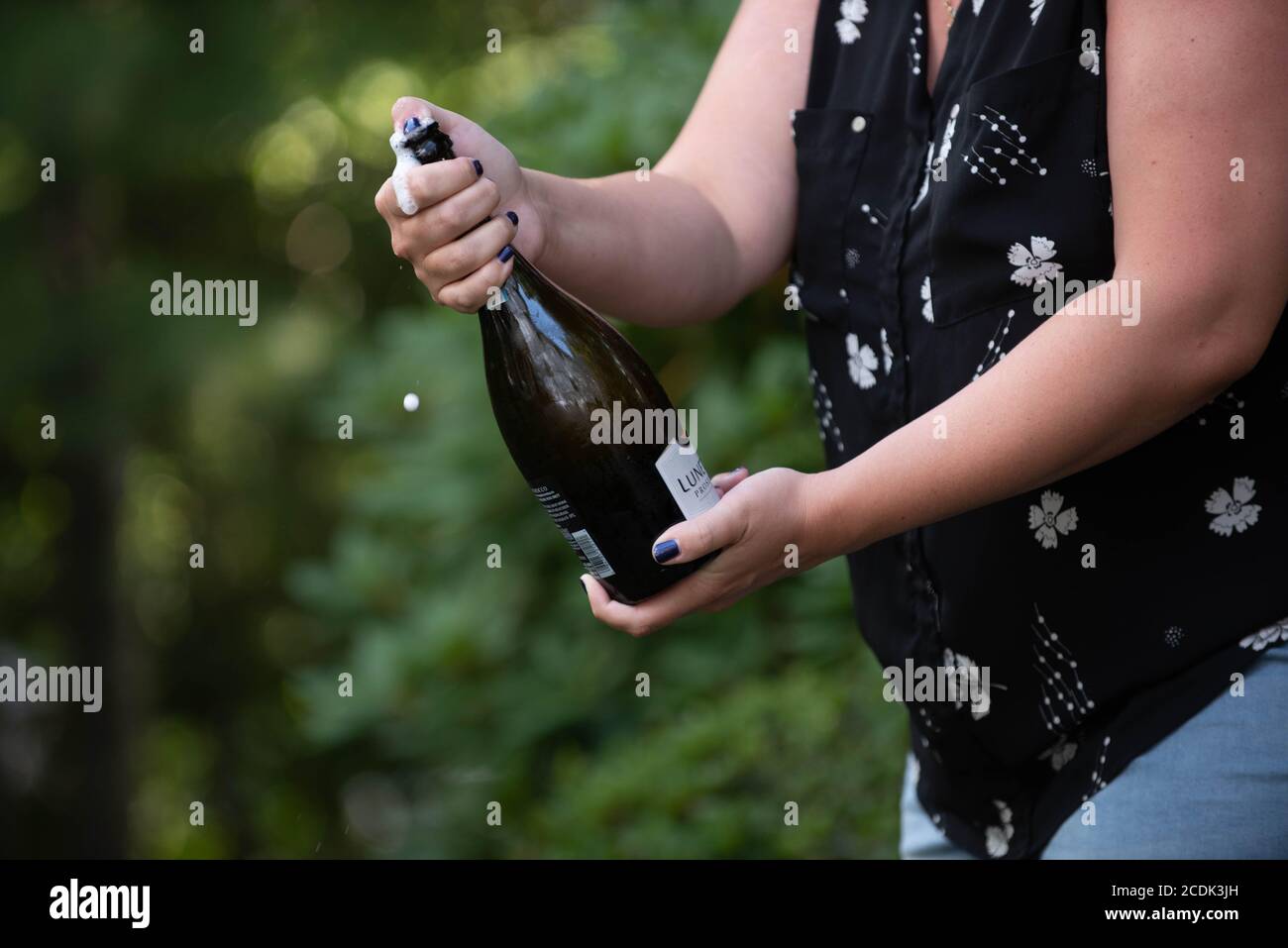 Une femme ouvre une bouteille de champagne à un fête de remise des diplômes Banque D'Images