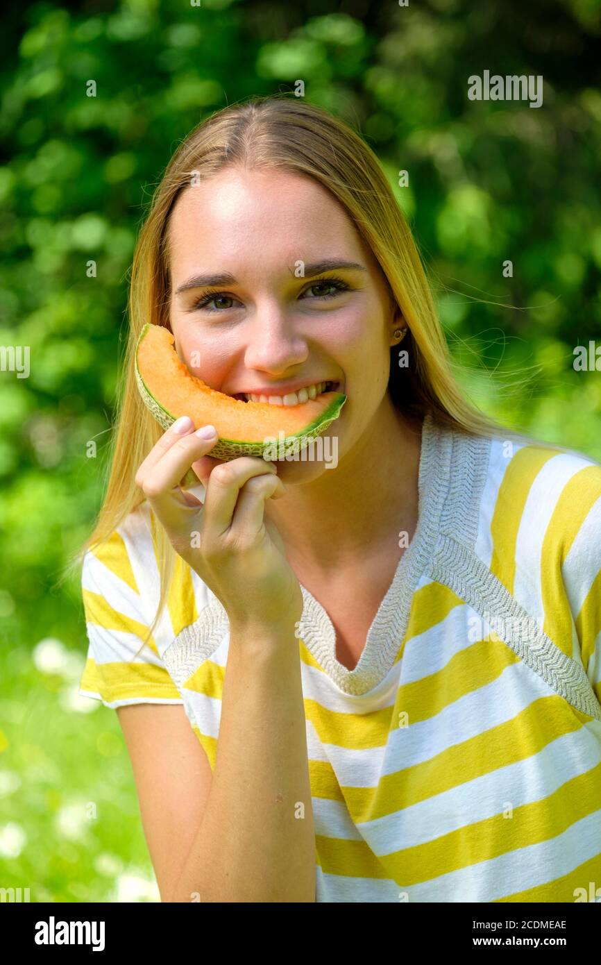 Portrait jeune femme blonde, piquant dans un melon, fruit, été, Bavière, Allemagne Banque D'Images