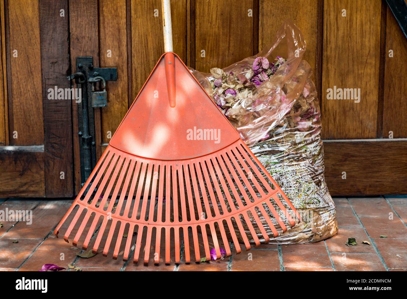 Sac en plastique rempli de feuilles sèches et de fleurs sèches recueillies avec et râteau d'orange prêt à être recyclé. Déchets de jardin recueillis lors du confinement de la covid-19. Banque D'Images