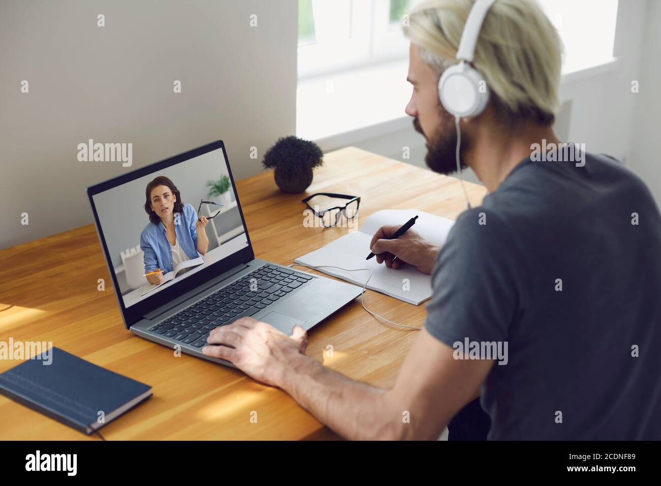 Formation et travail en ligne. Jeune homme assis à la maison à son bureau et utilisant la vidéoconférence sur ordinateur portable pour étudier et travailler. Banque D'Images