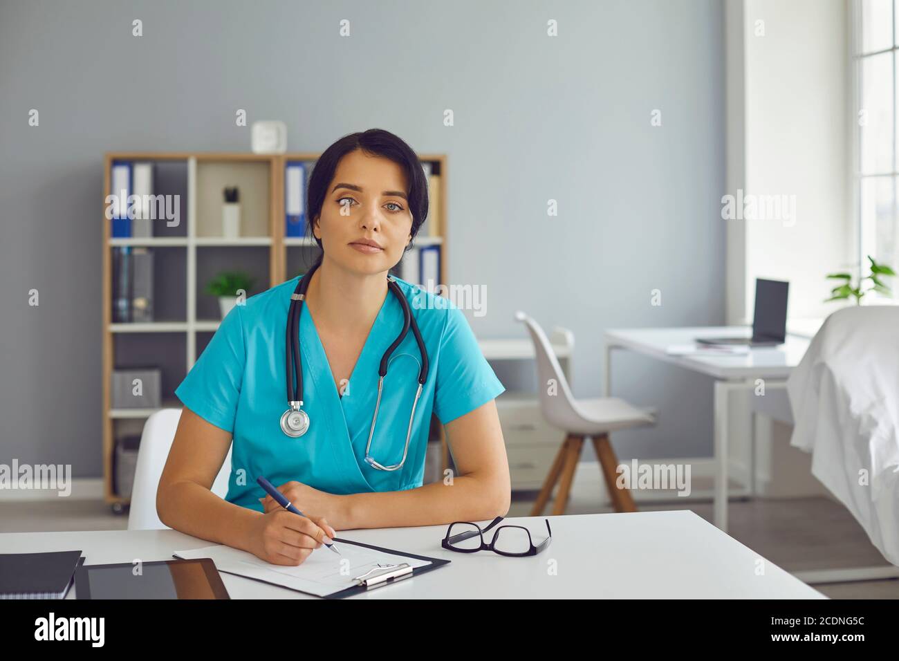 Femme médecin thérapeute assise dans le bureau de la clinique médicale, prenant des notes et regardant la caméra Banque D'Images