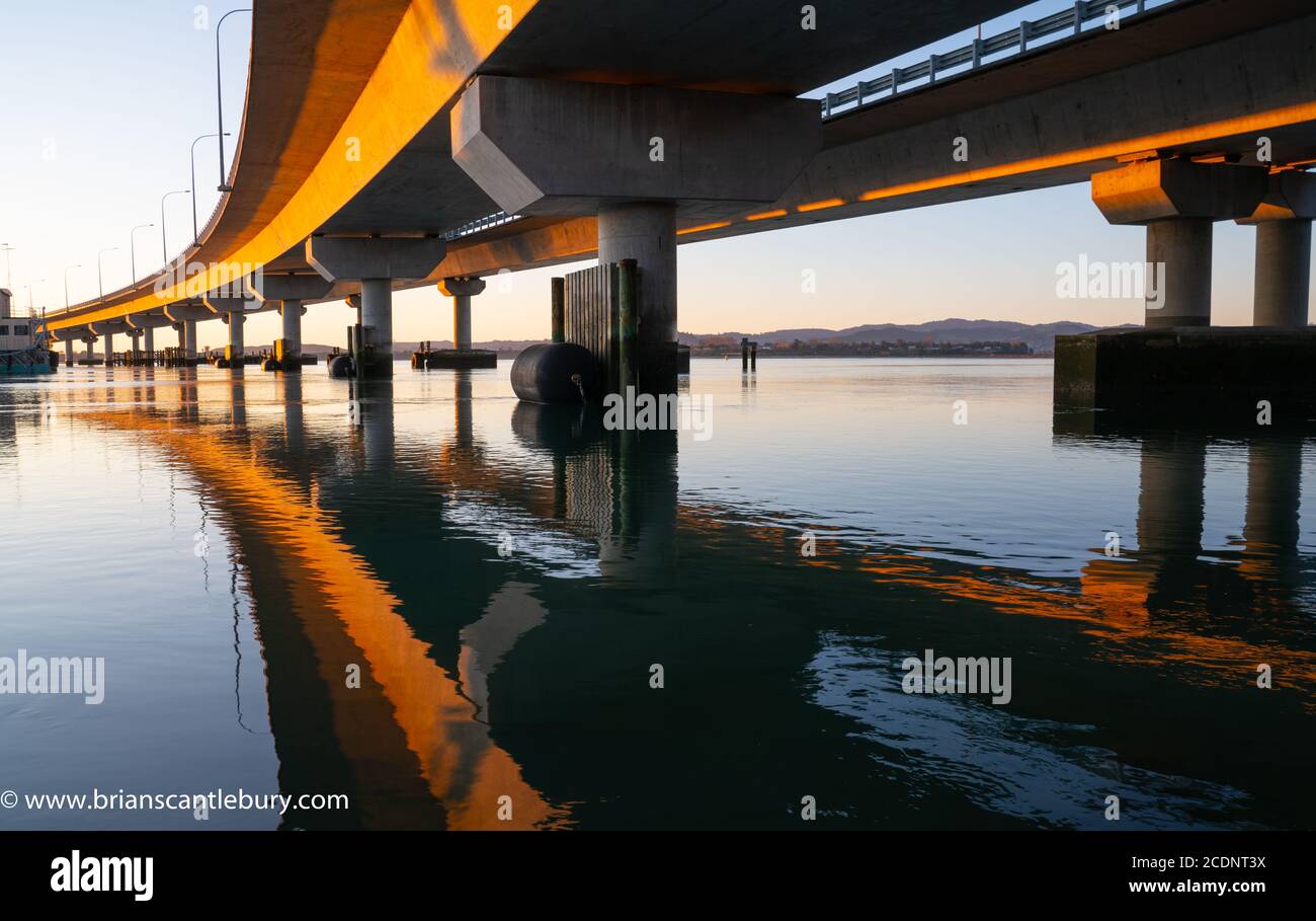 Le soleil du matin frappe à côté du pont du port de Tauranga dans la teinte dorée lignes de convergence principales reflétées en eau calme en dessous Banque D'Images