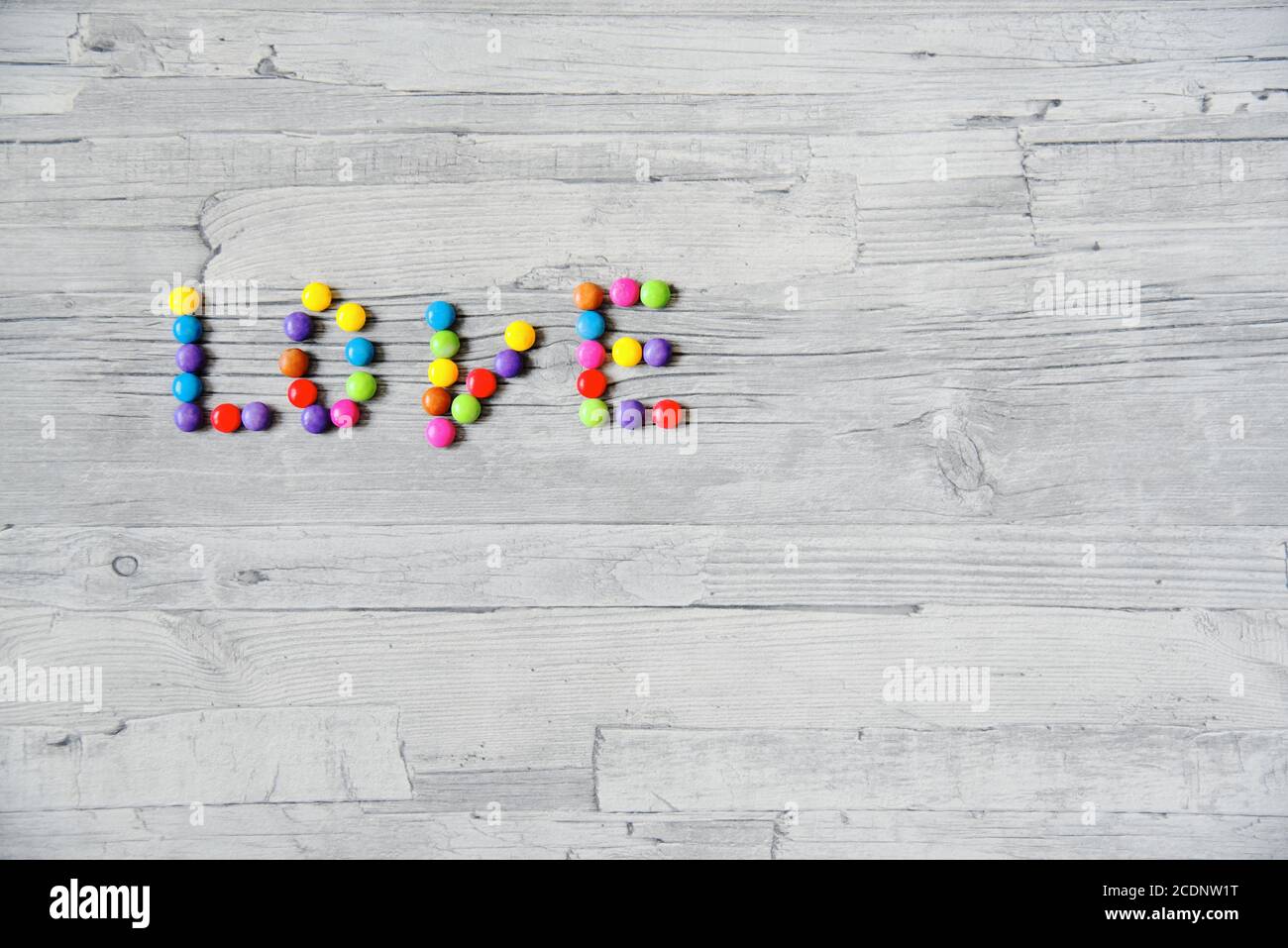 Le mot « amour » écrit avec des lentilles de chocolat colorées sur un fond en bois clair. Banque D'Images