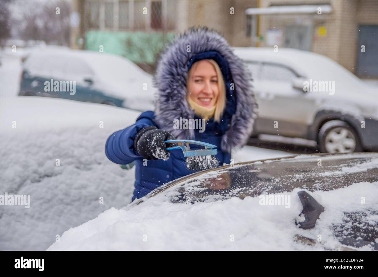 Défricher la neige de la voiture en hiver dans la cour avec une brosse Banque D'Images