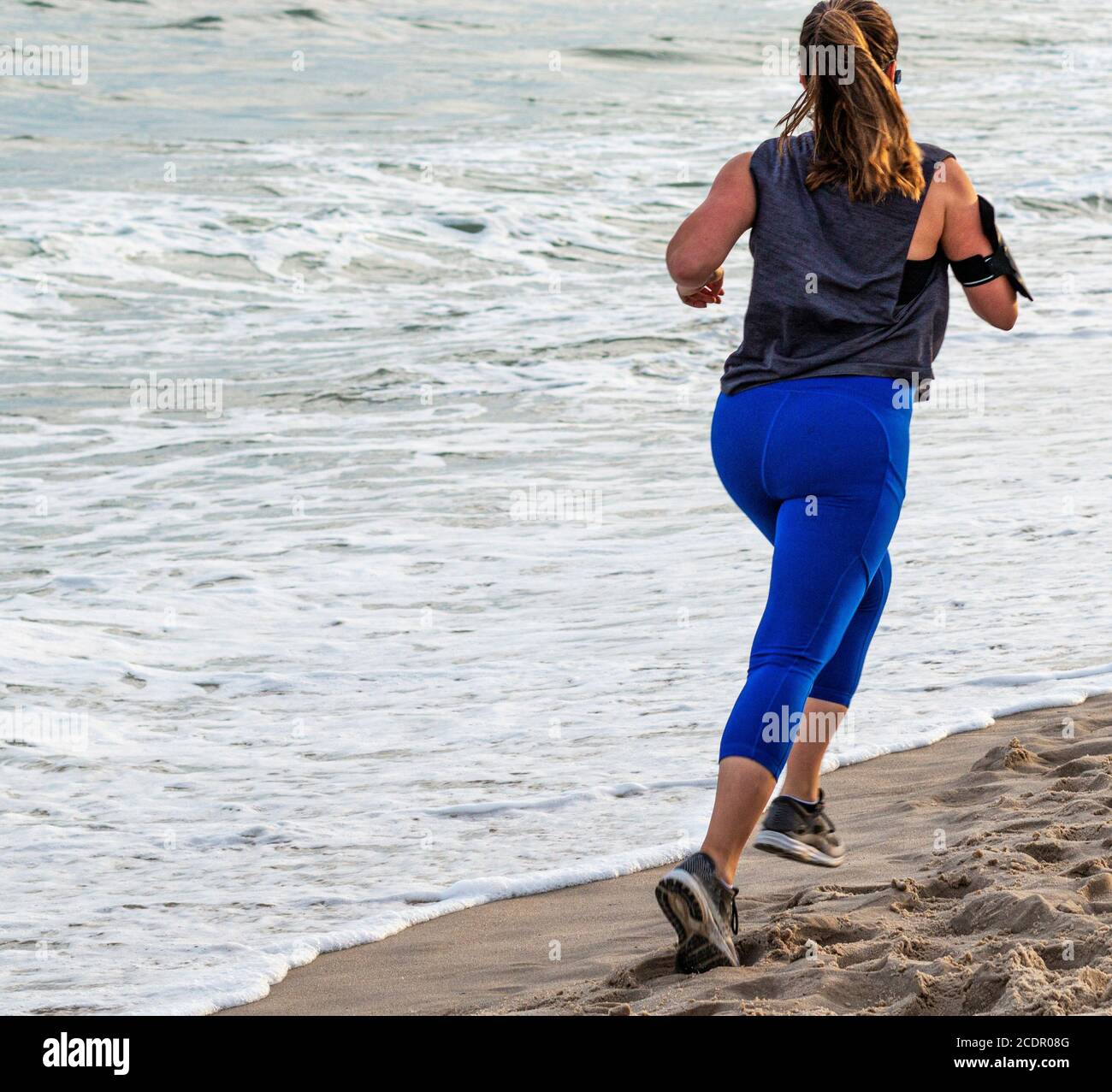 Une femme en spandex bleu court à la plage près de l'océan sur Fire Island. Banque D'Images