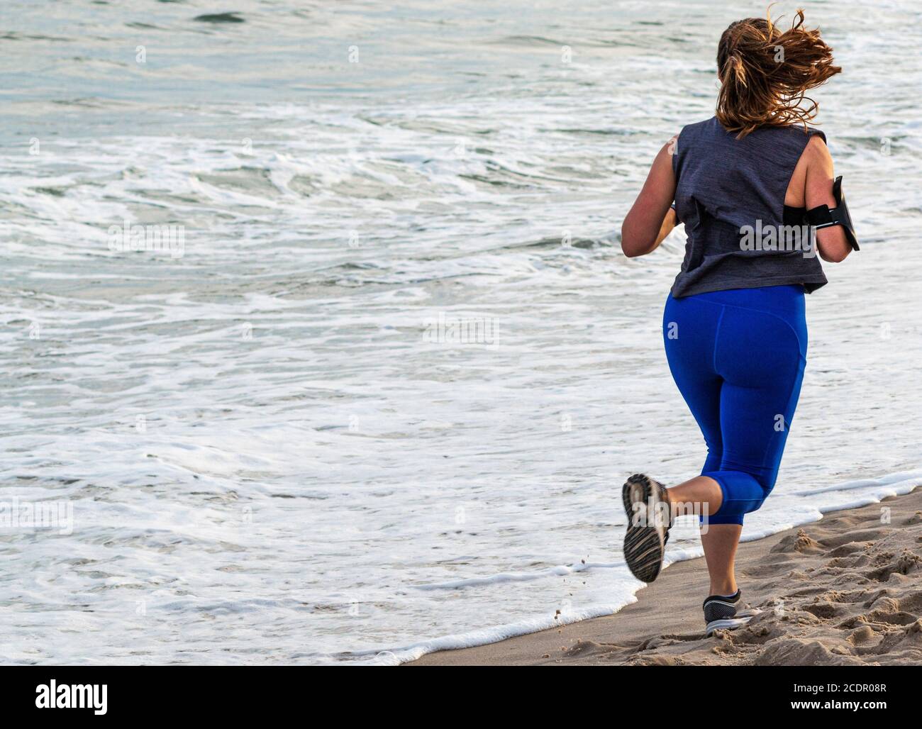 Vue arrière d'une femme qui court sur la plage au bord de l'eau sur le sable. Banque D'Images