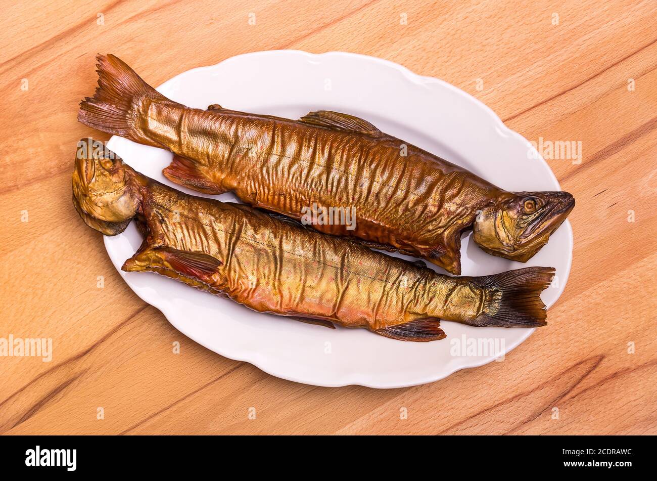 Deux poissons fumés, l'omble de fontaine, sur une assiette blanche sur une table en hêtre. Banque D'Images