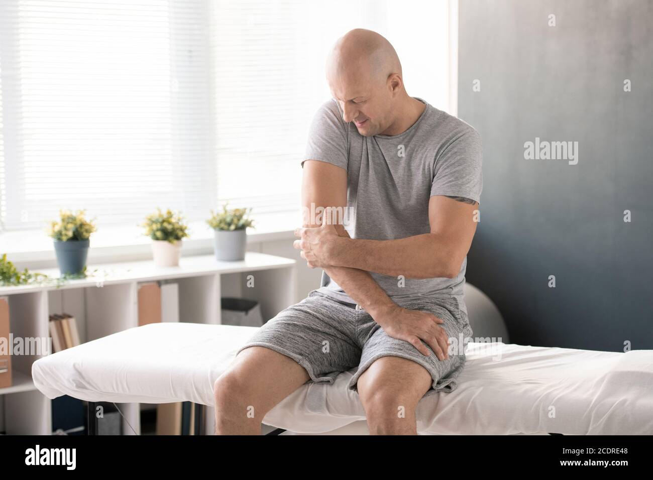 Homme chauve touchant le coude douloureux et essayant de le masser avant de faire de l'exercice Banque D'Images