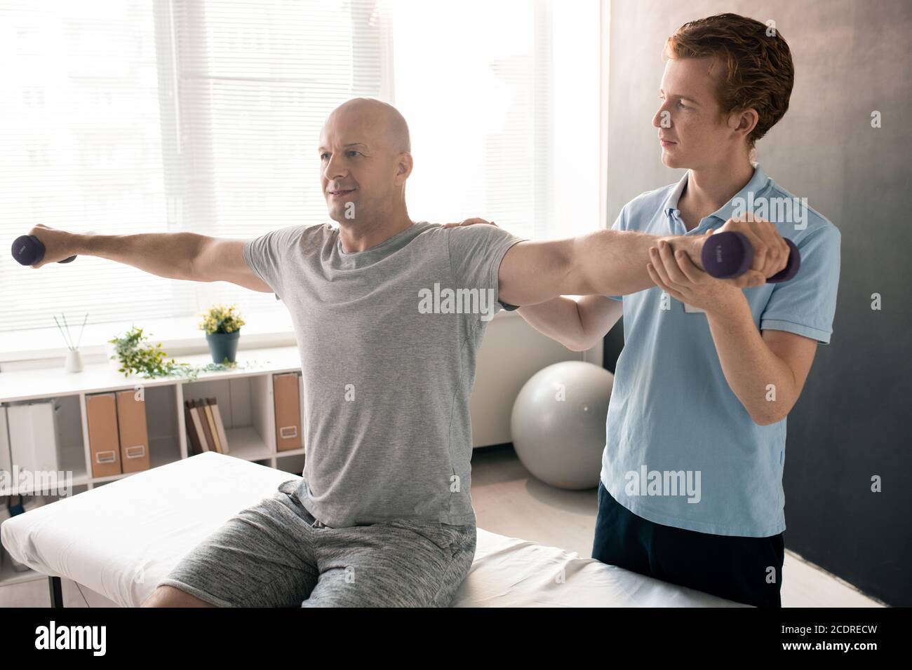 Jeune physiothérapeute en polo bleu tenant le bras étiré de patient Banque D'Images