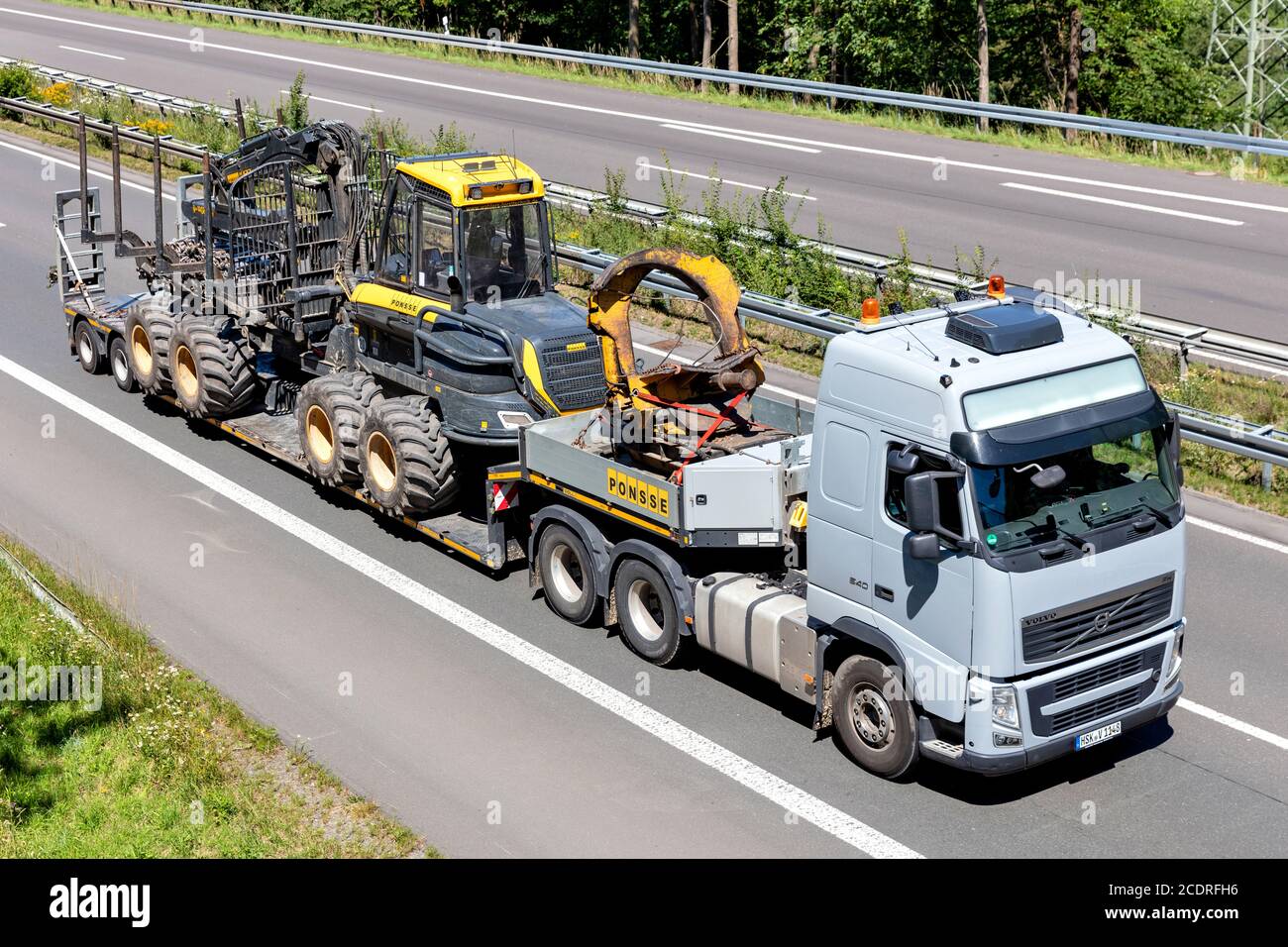 Camion à plateau Volvo FH Ponsee avec machine forestière sur autoroute. Banque D'Images