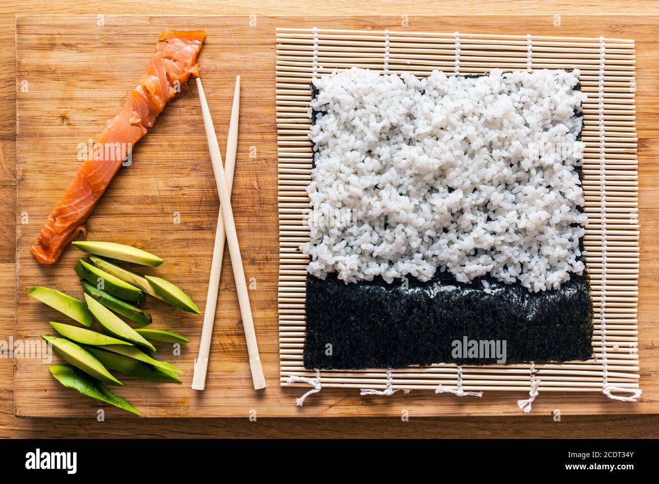 La préparation des sushis. Le saumon, avocat, riz et baguettes sur la table en bois. Banque D'Images