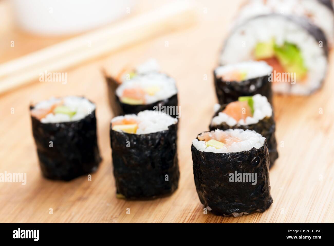 Petits pains à sushis avec saumon, avocat, riz aux algues et baguettes Banque D'Images