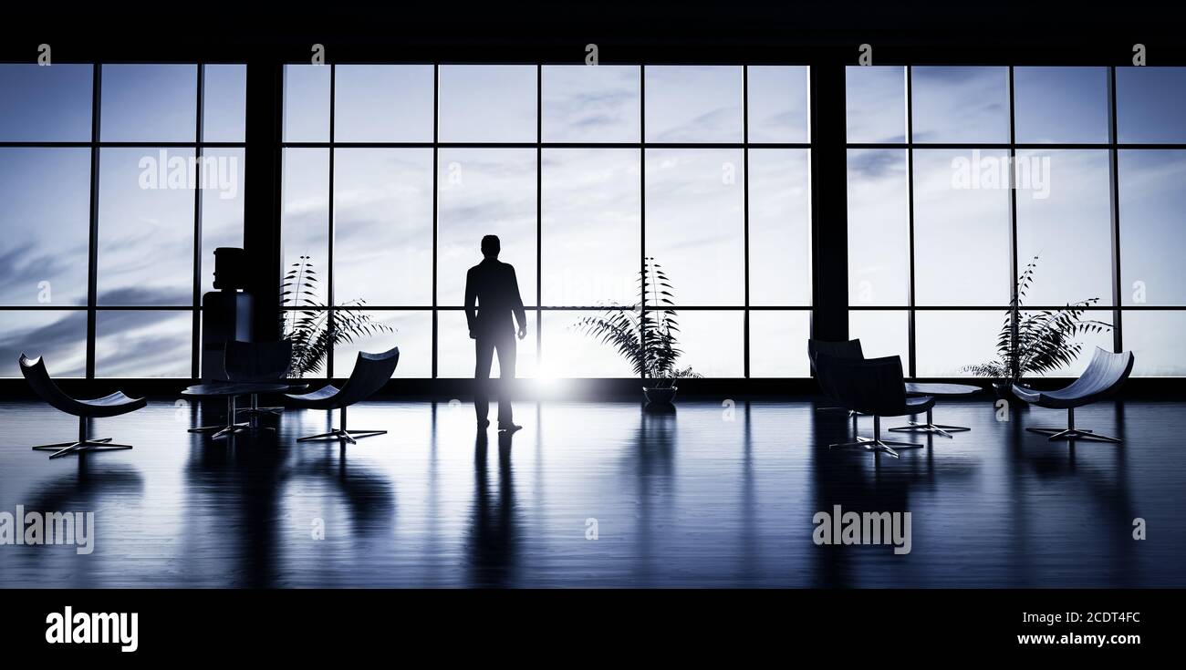 Homme d'affaires debout dans le bureau et regardant par la fenêtre au coucher du soleil. Banque D'Images