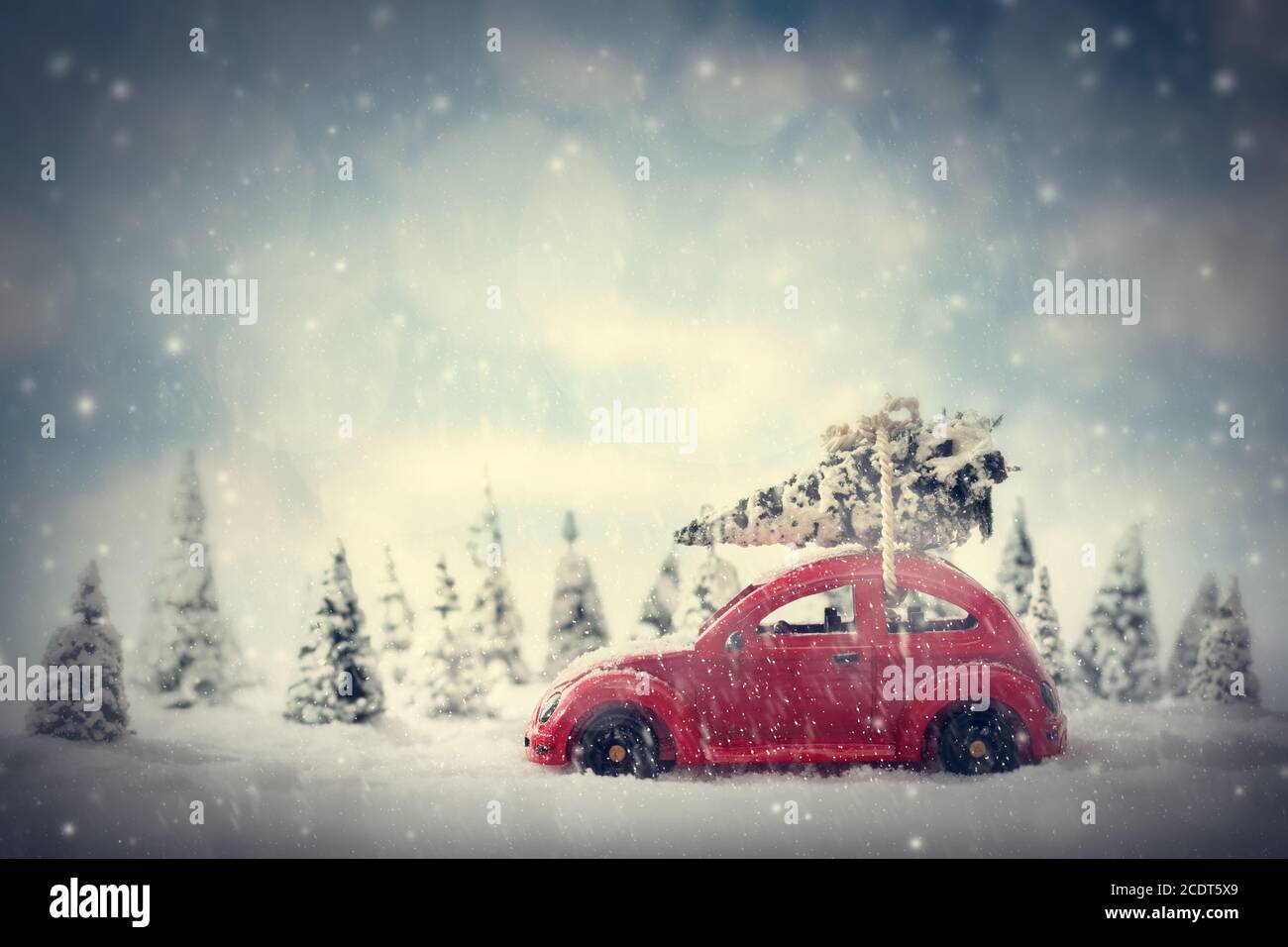 Voiture de jouet rétro transportant un petit arbre de Noël. Paysage de conte de fées avec neige et forêt. Banque D'Images