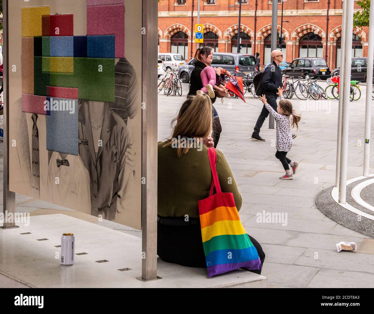 Jeune femme assise sur un banc avec sac fourre-tout de couleur arc-en-ciel, Kings Cross, Londres, Angleterre Banque D'Images