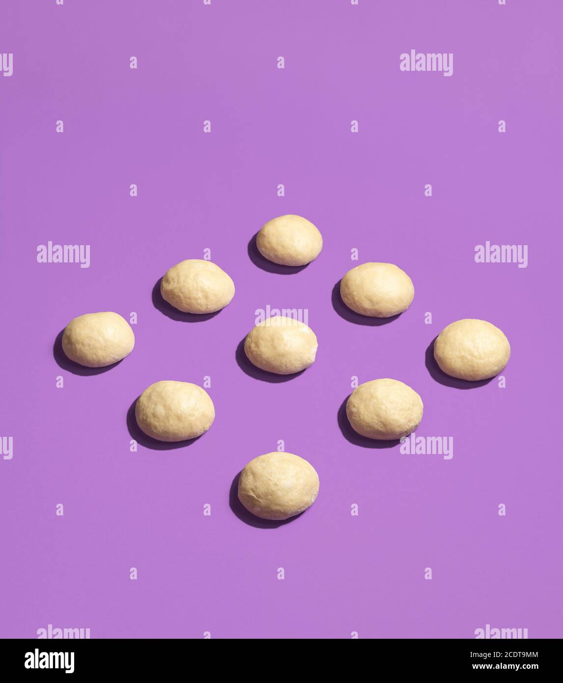 Pâte de pains crus affichée symétriquement sur un fond violet sans couture. Boulettes de pâte non cuites. Processus de levain et de façonnage de la pâte. Cuisson du pain. Banque D'Images