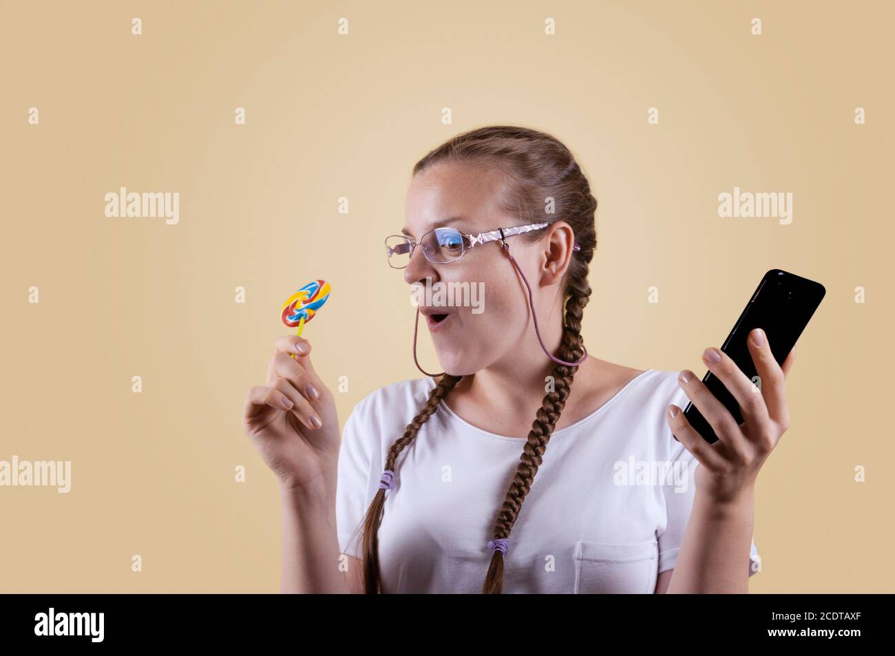 La fille regarde le téléphone. La fille tient le téléphone. Fille avec picots. La fille est prise sur fond jaune. La fille est surprise b Banque D'Images