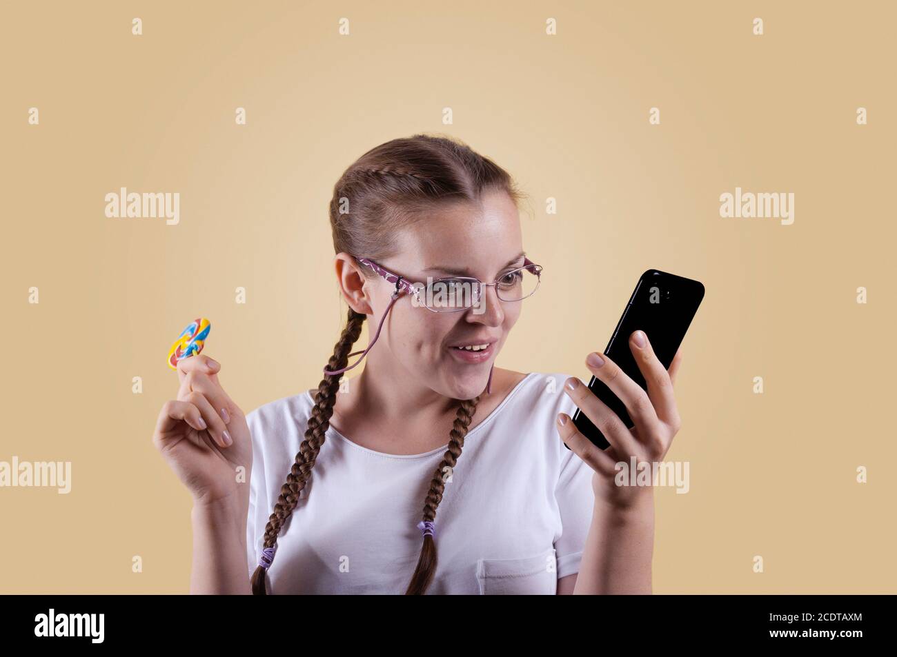 La fille regarde le téléphone. La fille tient le téléphone. Fille avec picots. La fille est prise sur fond jaune. La fille est surprise b Banque D'Images
