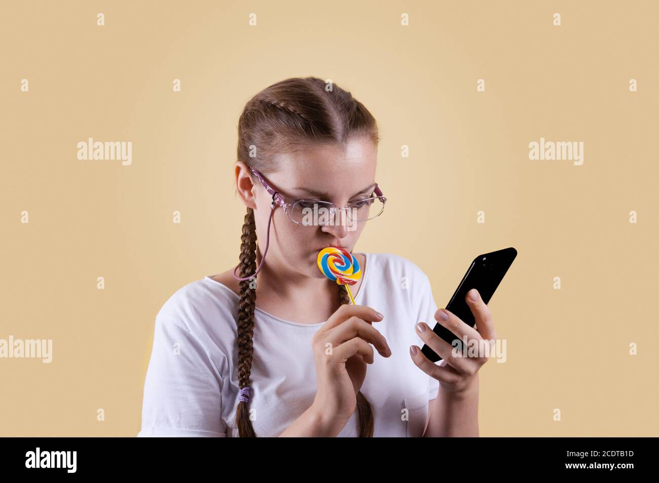 La fille regarde le téléphone. La fille tient le téléphone. Fille avec picots. La fille est prise sur fond jaune. La fille a l'air bien pensée Banque D'Images