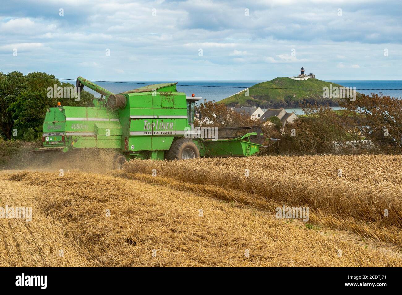 Ballycotton, East Cork, Irlande. 29 août 2020. Une moissonneuse-batteuse Deutz-Fahr Topliner 4080 HTS exploitée par des entrepreneurs Barry et John Flavin coupe du blé d'hiver sur la ferme Ballycotton d'Alan et John Dunne lors d'une journée ensoleillée à East Cork, avec Ballycotton Lighthouse en arrière-plan. Crédit : AG News/Alay Live News Banque D'Images