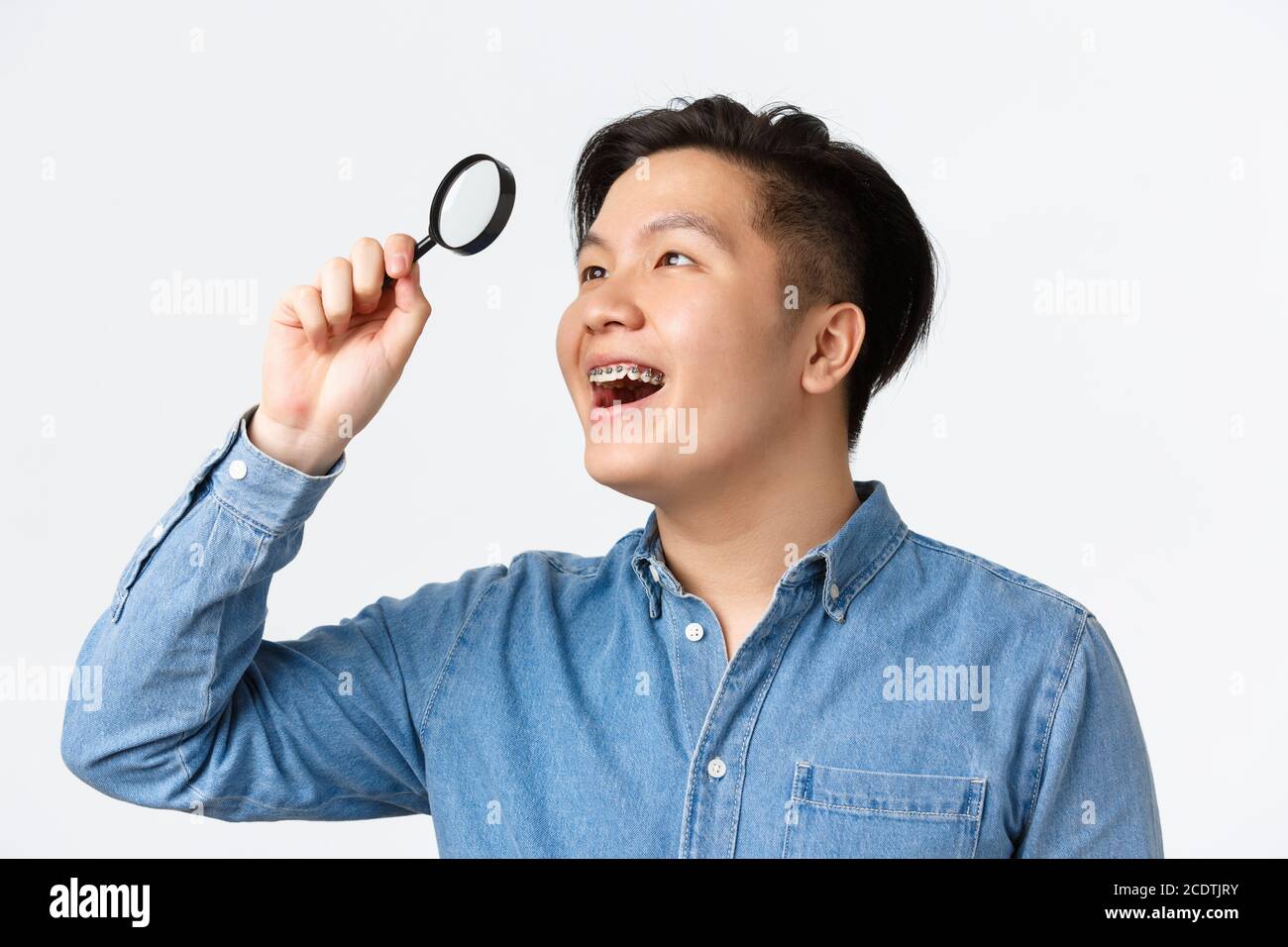 Gros plan d'un jeune homme asiatique amusant et excité avec des bretelles,  souriant satisfait, trouvé quelque chose d'intéressant, regardant à travers  la loupe à l'empeigne Photo Stock - Alamy
