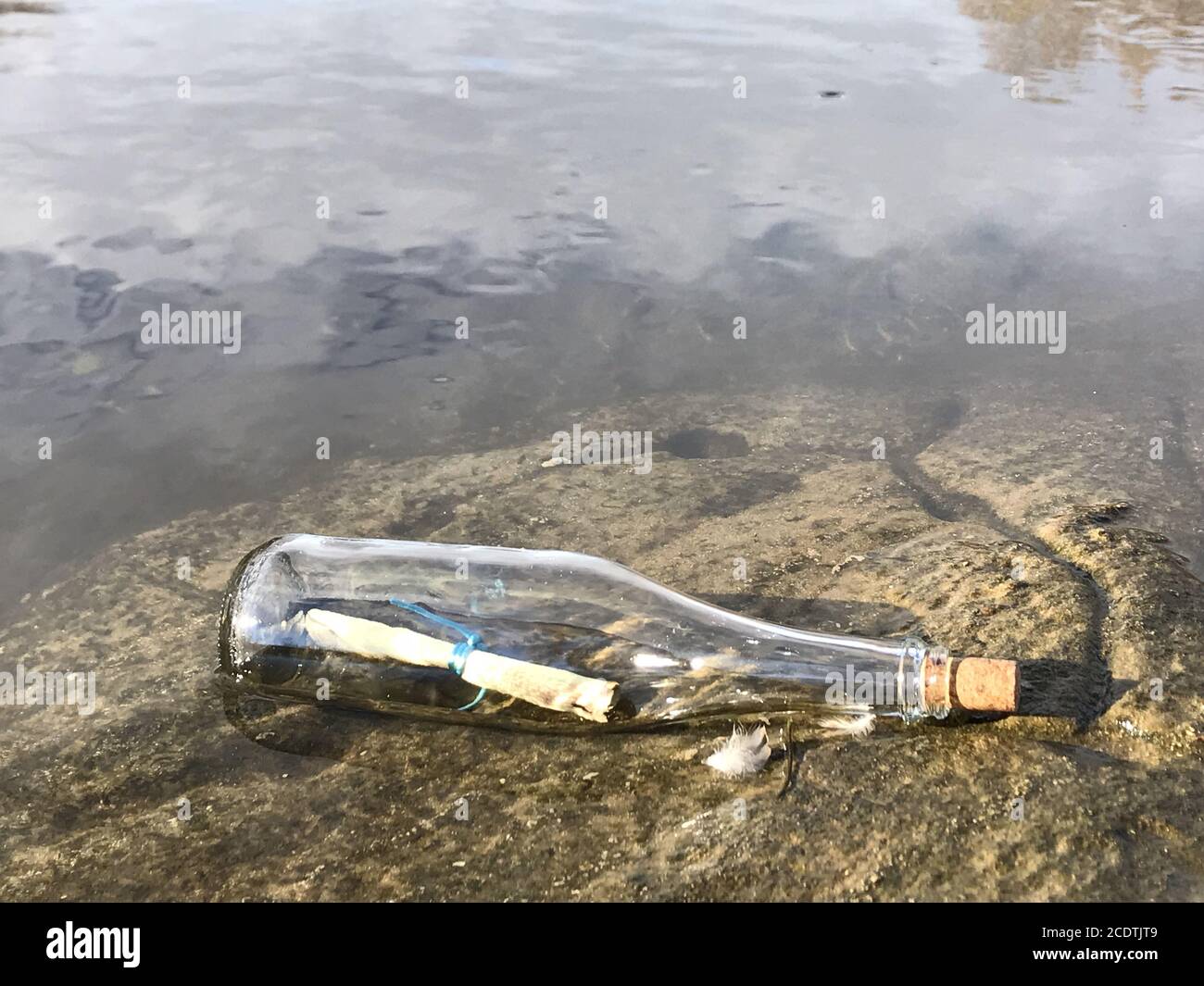 Message dans une bouteille de cristal à la plage avec de l'eau et du sable Banque D'Images