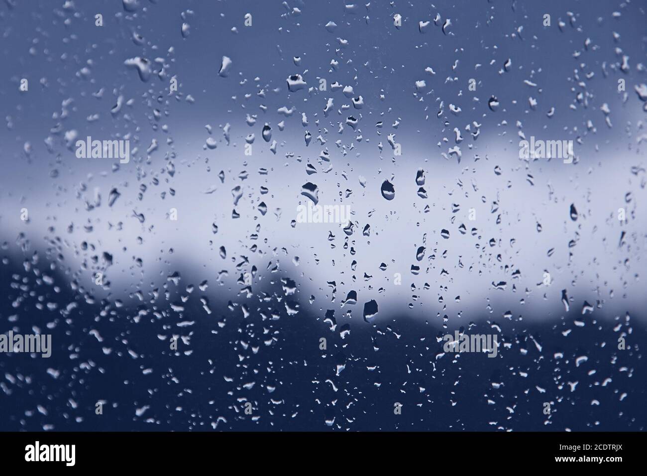 Fenêtre humide par temps pluvieux d'automne. Gouttes d'eau sur le verre, tons bleus Banque D'Images