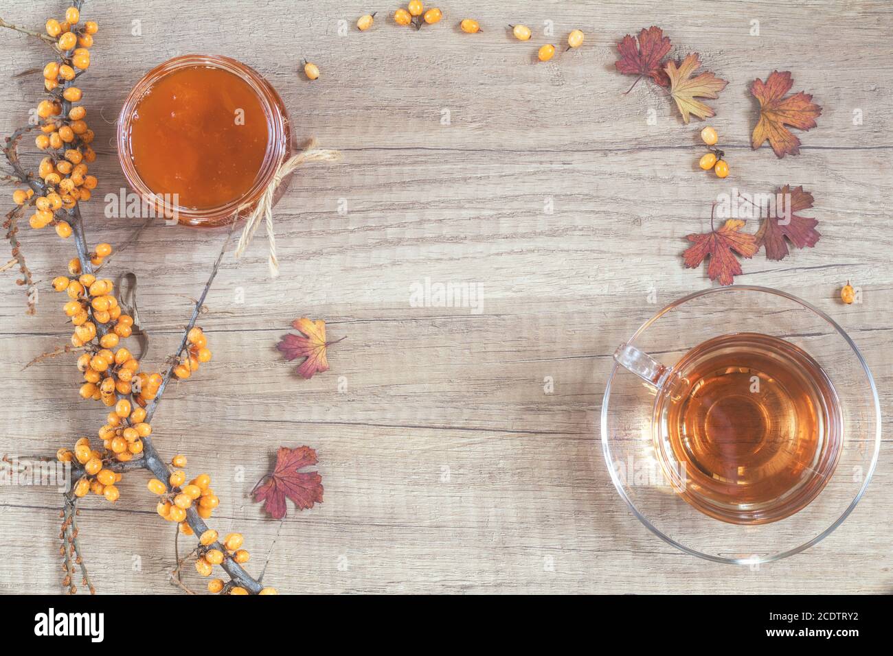 Concept de boisson chaude santé d'automne. Branche d'argousier commun avec baie, tasse de thé, jarre de confiture sur fond de bois clair Banque D'Images