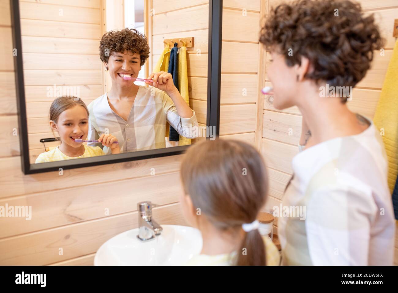 Bonne jeune femme brunette et sa petite fille mignonne se brossant dents ensemble Banque D'Images