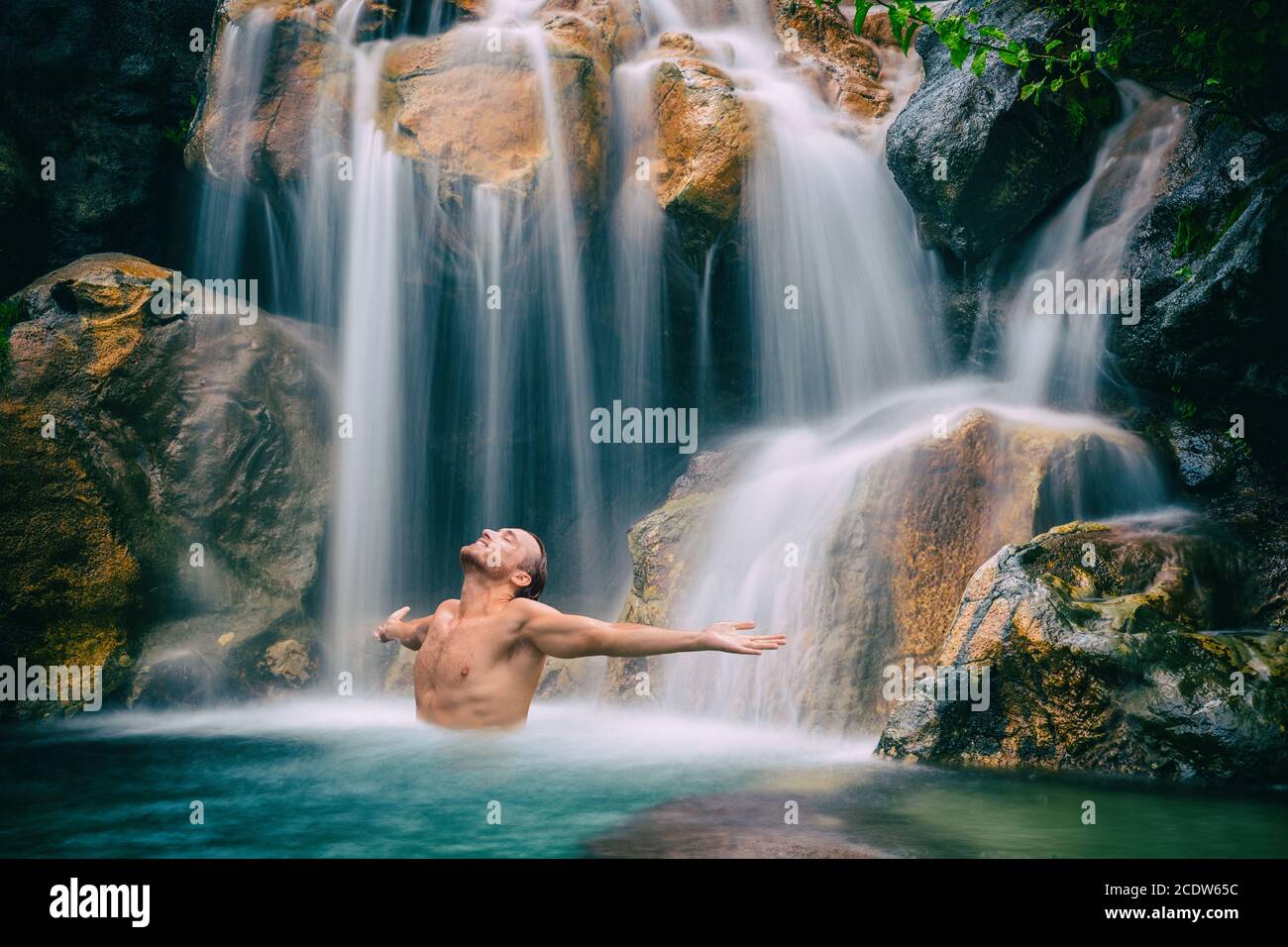 Homme se détendant avec la liberté bras ouverts dans la cascade dans la nature tropicale. Concept de spa bien-être dans la nature des vacances Banque D'Images