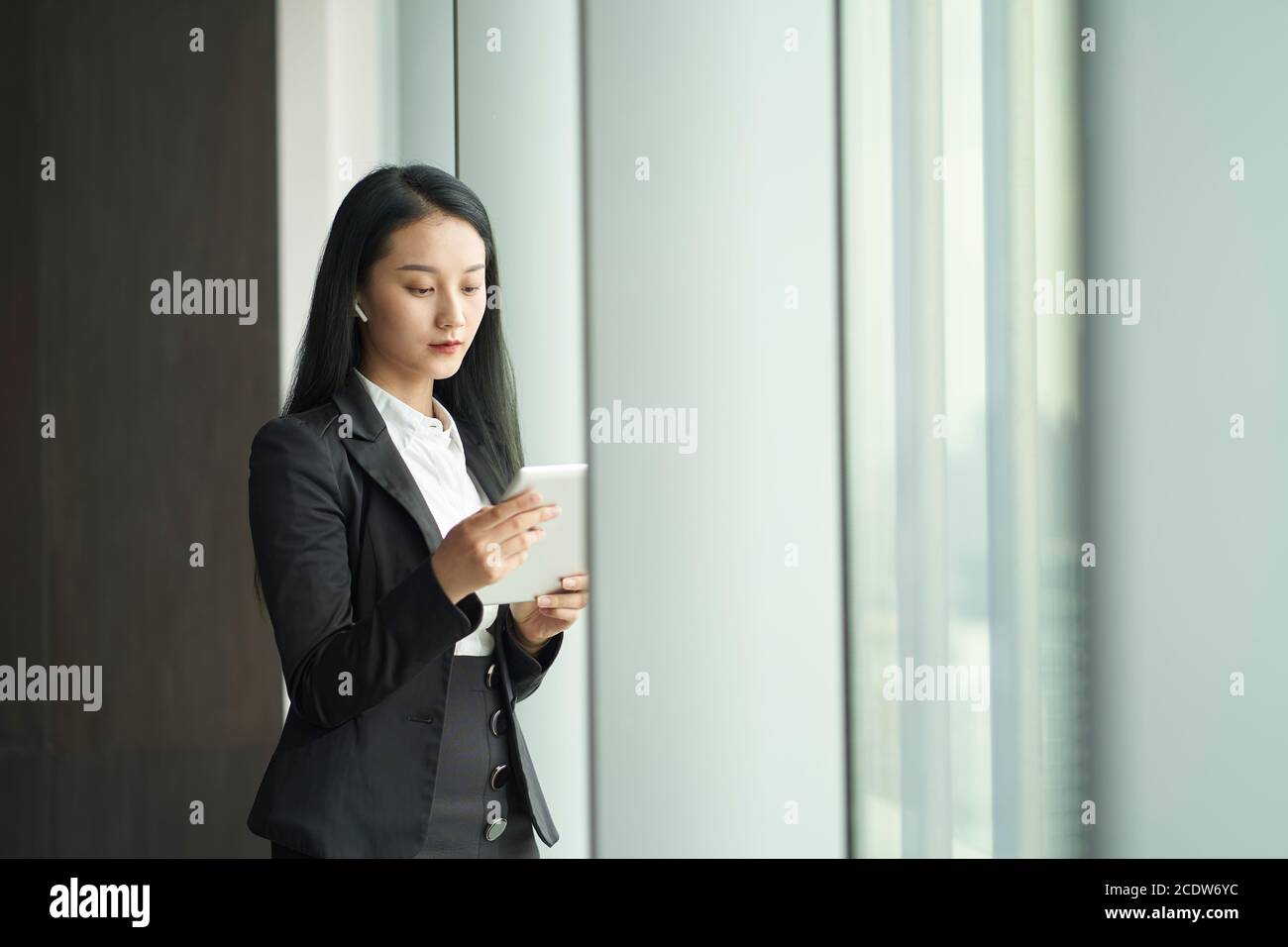 jeune femme d'affaires asiatique debout devant une fenêtre regardant le numérique tablette au bureau Banque D'Images