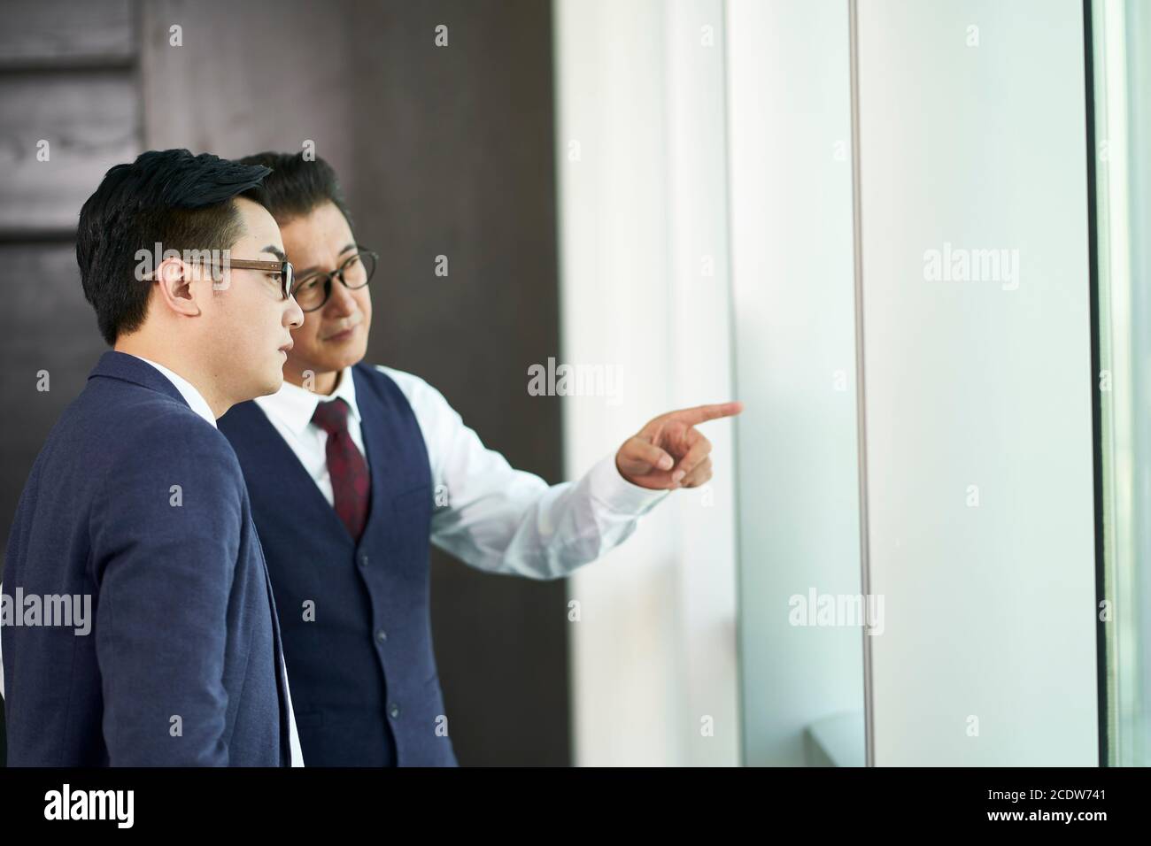 deux dirigeants d'entreprises asiatiques debout sous les fenêtres qui parlent au bureau Banque D'Images