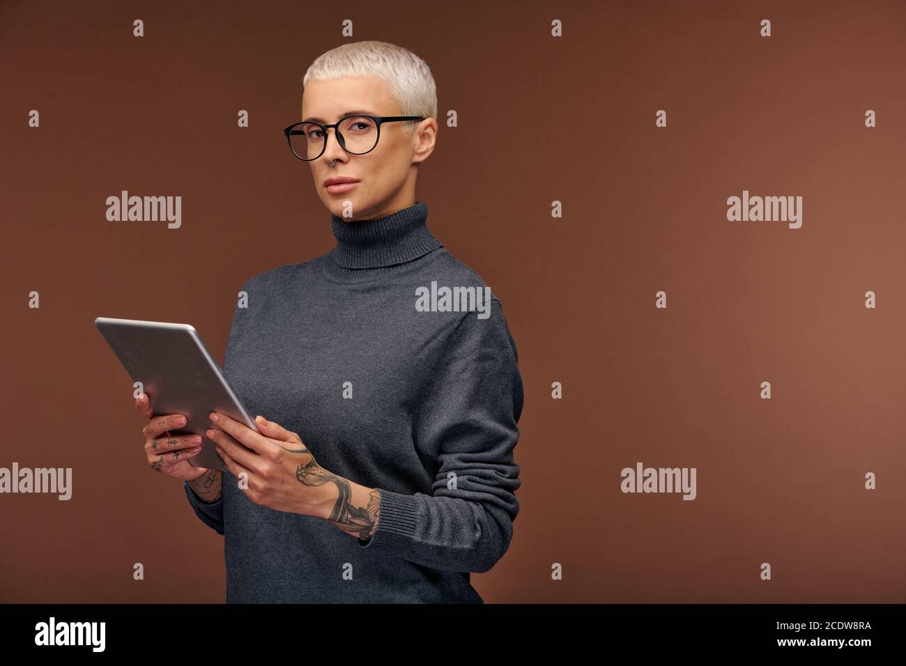 Jeune femme d'affaires élégante en pull-over gris foncé et lunettes de vue utilisant tablette Banque D'Images