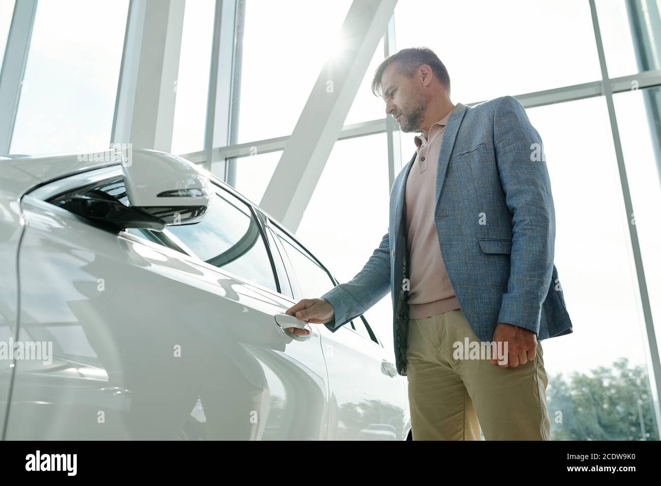 Jeune homme contemporain en tenue décontractée élégante debout par le nouveau blanc voiture Banque D'Images