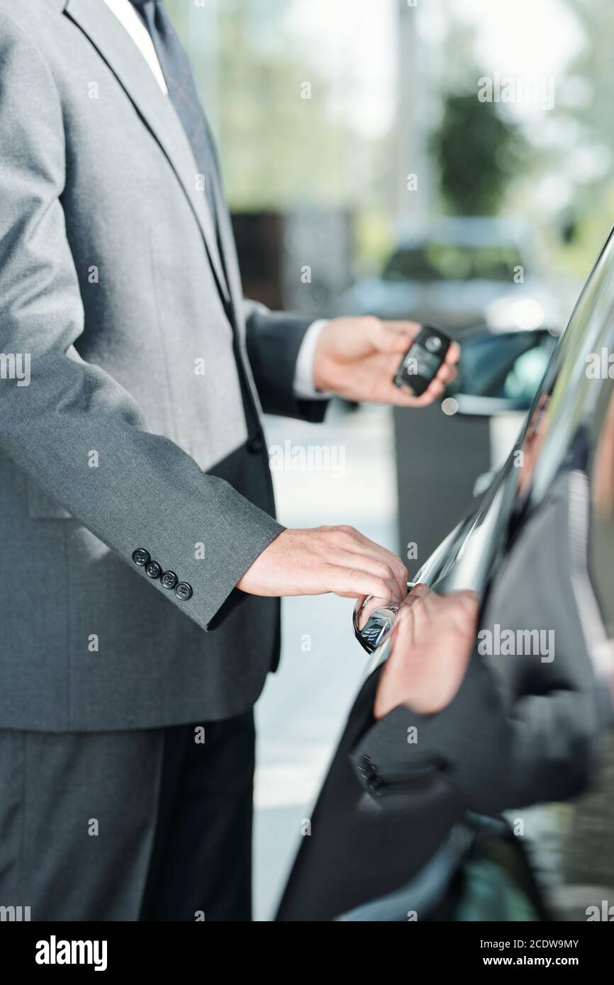 Jeune élégant vendeur de nouvelles voitures en costume utilisant la télécommande commande d'ouverture de la porte Banque D'Images
