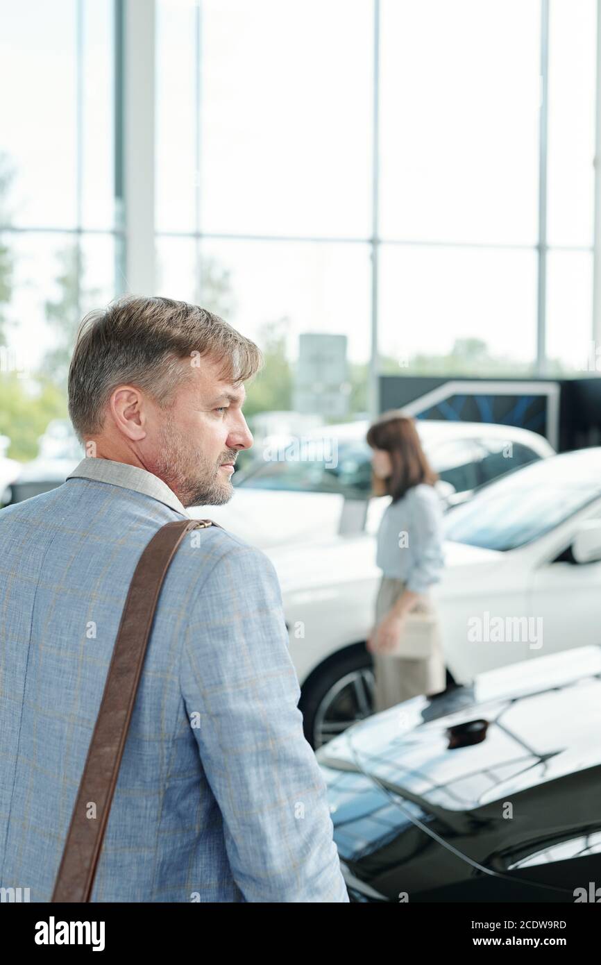 Vue arrière de l'homme mature dans une veste bleue debout avant d'une luxueuse voiture noire Banque D'Images