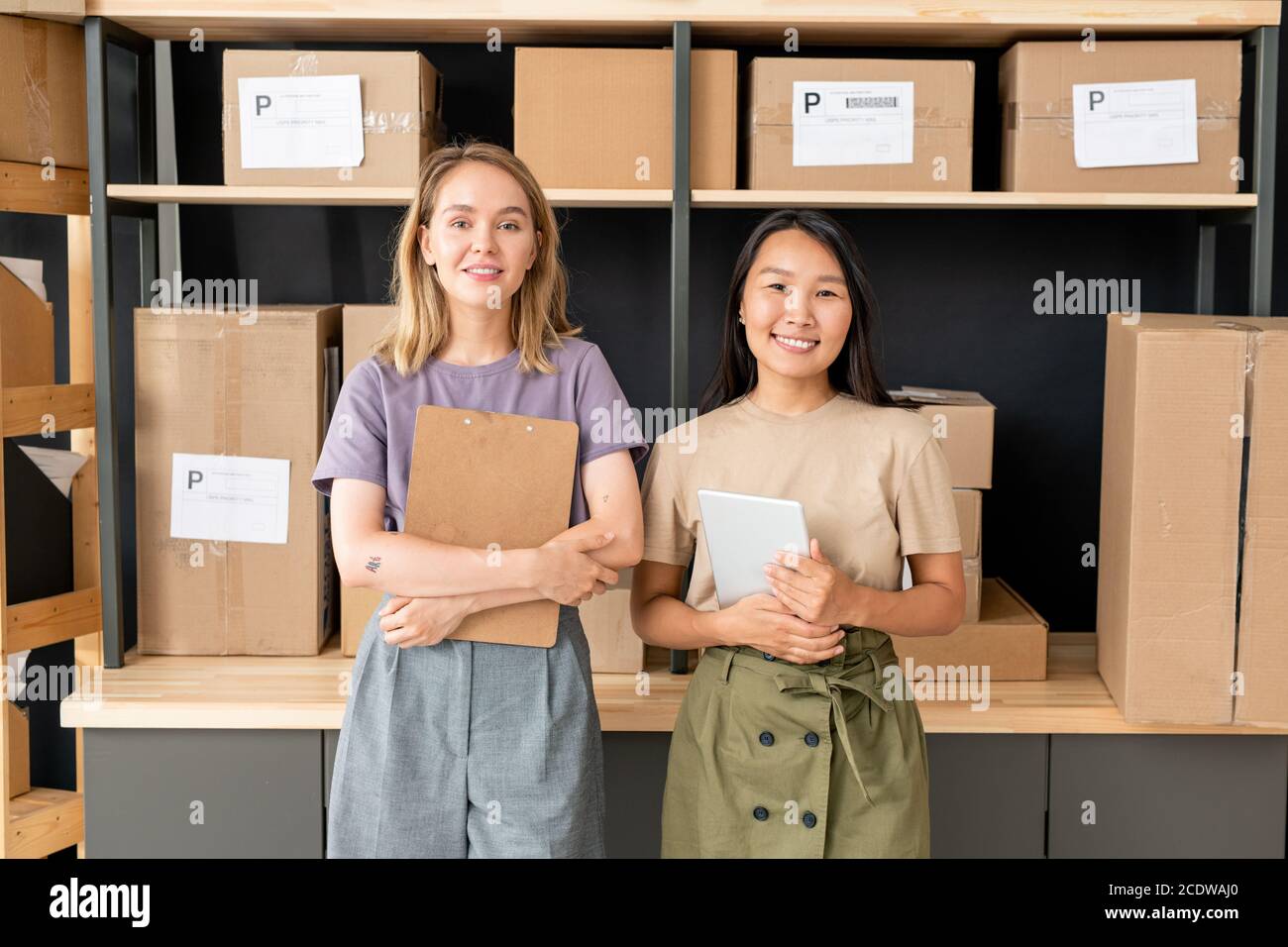 Deux jeunes travailleurs joyeux de la salle de stockage de la boutique en ligne en vous tenant par des étagères Banque D'Images