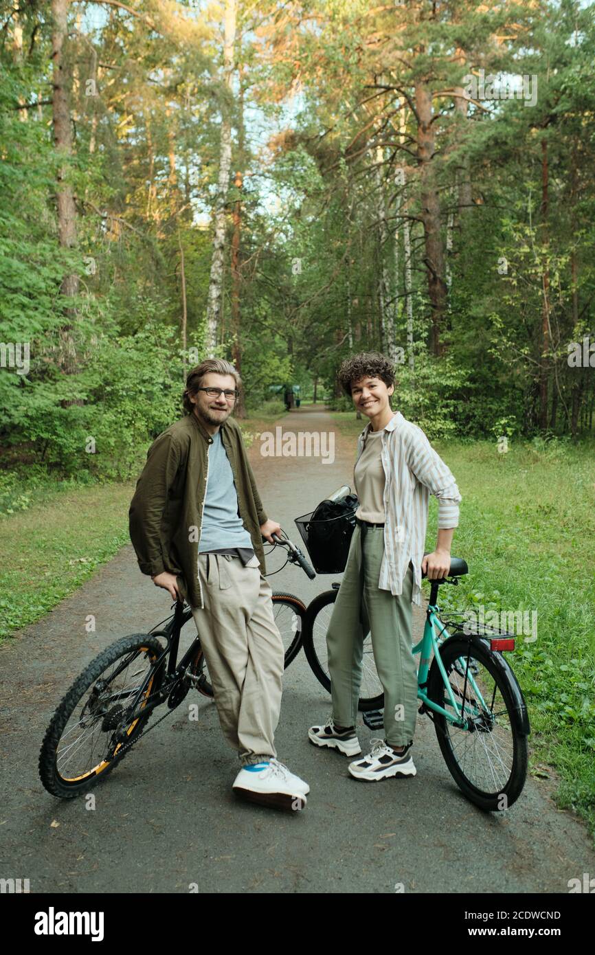 Jeune couple joyeux avec des vélos debout entre les arbres en face de la caméra Banque D'Images