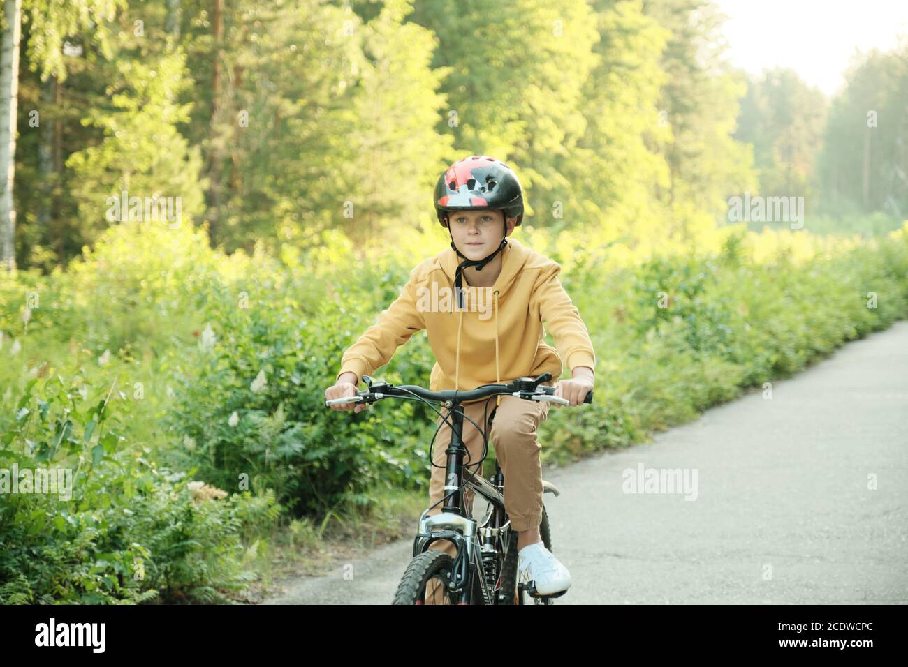 Écolier en vêtements décontractés et casque de protection à vélo neuf le long route Banque D'Images