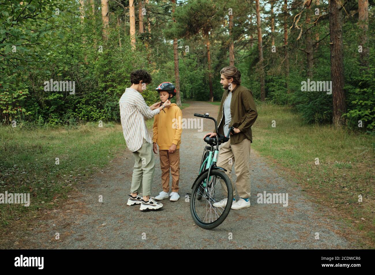 Jeune mère attentive aidant son fils à attacher des ceintures de casque de sport Banque D'Images