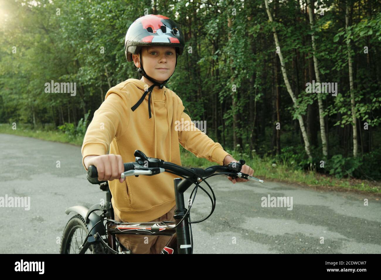 Jeune à capuche jaune et casque de protection tenu par des poignées de vélo Banque D'Images
