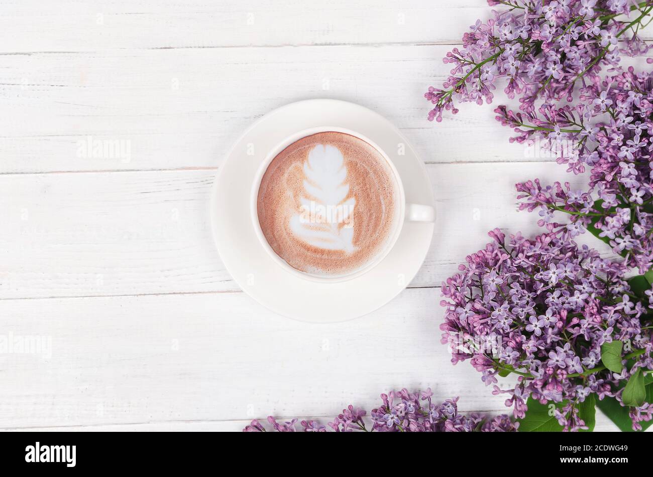 Lilas, café avec art latte sur table en bois clair. Matin romantique. Pose à plat Banque D'Images