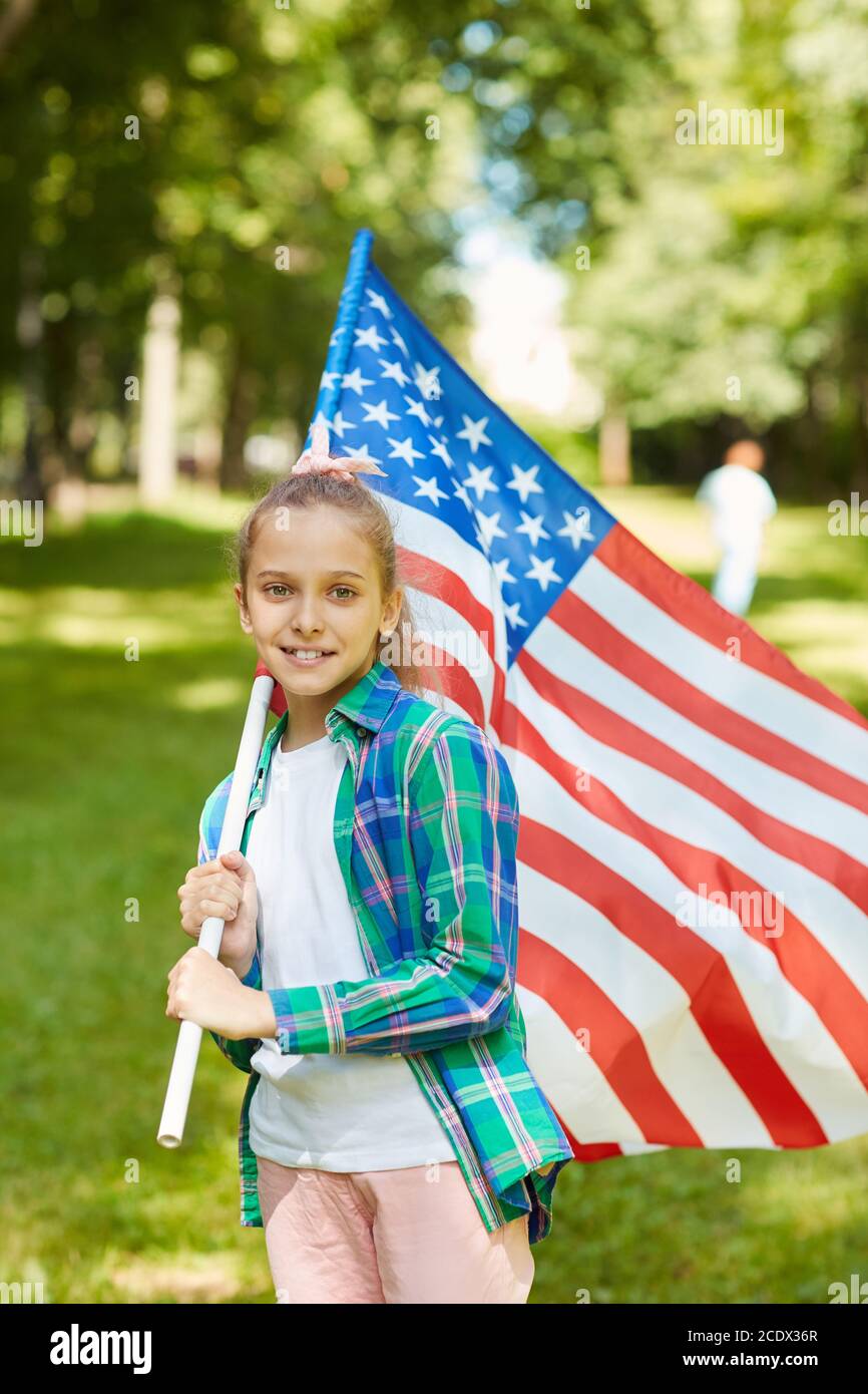 Portrait vertical à la taille d'une adolescente souriante portant un drapeau américain tout en se tenant à l'extérieur, au soleil, dans un espace de copie Banque D'Images