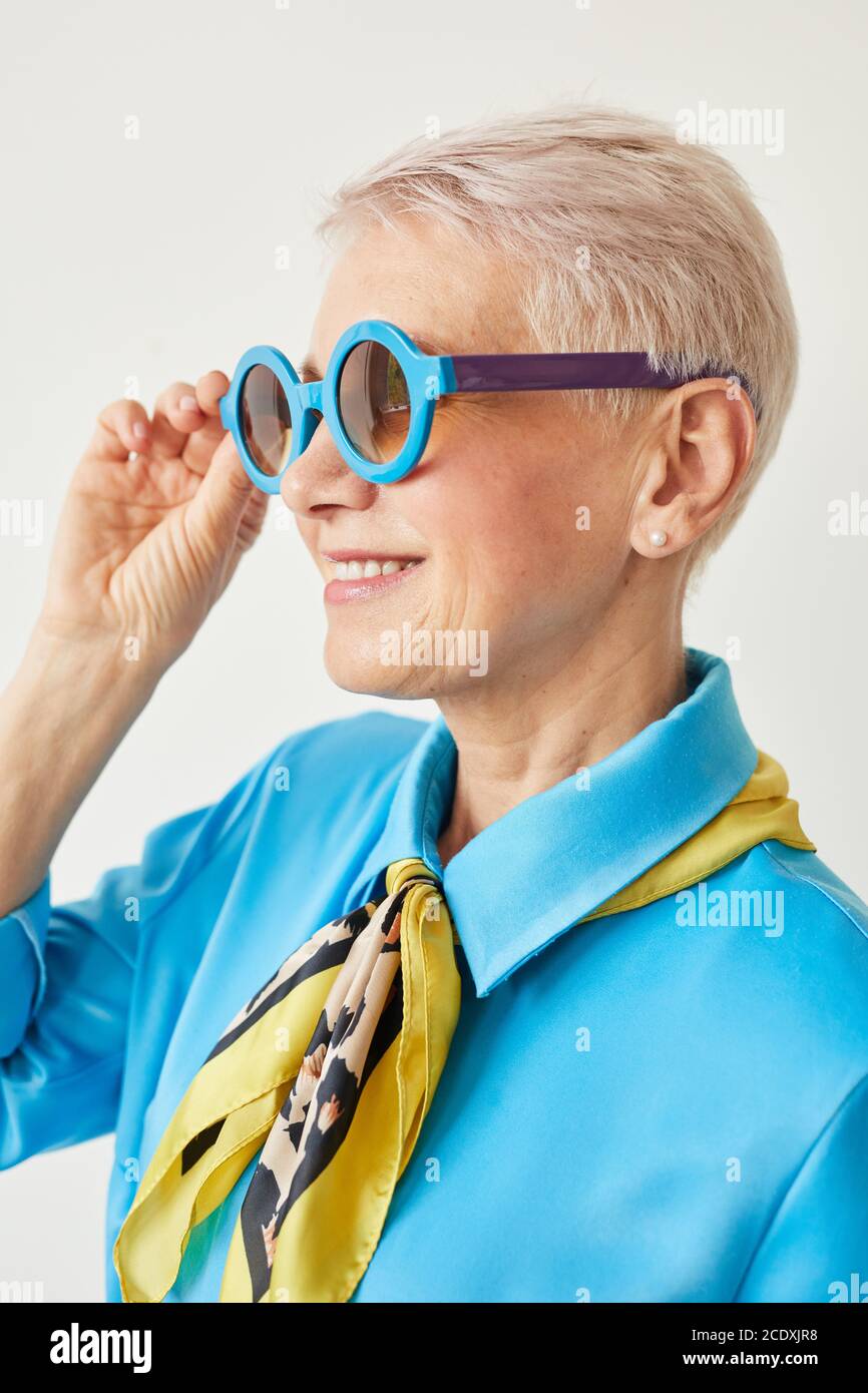 Élégante femme âgée avec cheveux courts blonds portant des lunettes de soleil et souriant isolé sur fond blanc Banque D'Images