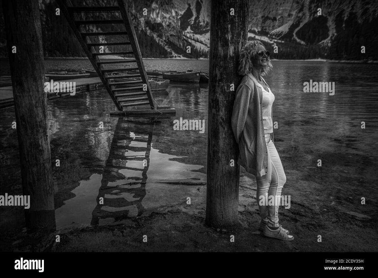 Portrait noir et blanc d'une femme brésilienne blonde souriante devant les eaux cristallines du lac Braies, Tyrol du Sud, Italie Banque D'Images