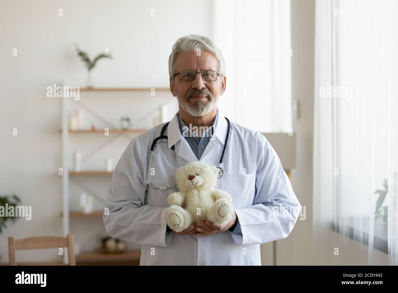 Tête de prise de vue portrait pédiatre mature tenant un ours en peluche Banque D'Images