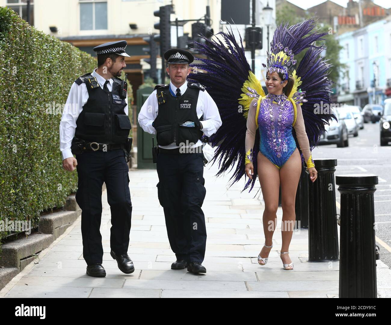 Les policiers en patrouille s'engagent dans une conversation avec l'instructeur de pilates Juliana Campos alors qu'elle pose dans son costume de carnaval à Notting Hill, Londres, sur ce qui aurait été le week-end du Carnaval de Notting Hill, après l'annulation du carnaval de 2020 en raison de la pandémie du coronavirus, les événements sont diffusés en ligne. Banque D'Images