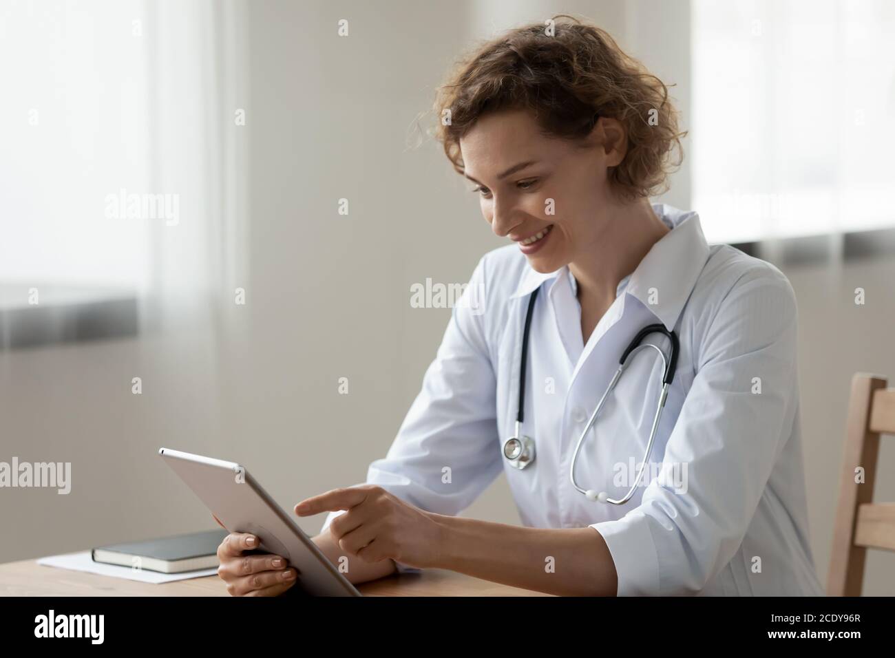 Jeune femme souriante médecin utilisant une tablette numérique, assis au bureau Banque D'Images