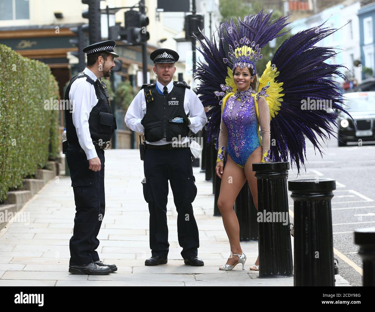 Les policiers en patrouille s'engagent dans une conversation avec l'instructeur de pilates Juliana Campos alors qu'elle pose dans son costume de carnaval à Notting Hill, Londres, sur ce qui aurait été le week-end du Carnaval de Notting Hill, après l'annulation du carnaval de 2020 en raison de la pandémie du coronavirus, les événements sont diffusés en ligne. Banque D'Images